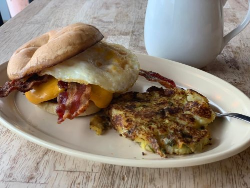 A breakfast plate featuring a bacon and egg sandwich with cheese, alongside a serving of hash browns and a coffee mug.