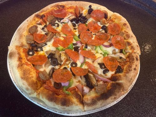 A freshly baked pizza topped with pepperoni, sausage, olives, mushrooms, and green peppers on a golden crust.