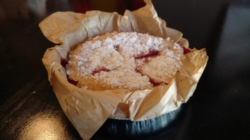 A round pastry with a golden crust, topped with powdered sugar and sitting in crumpled parchment paper.