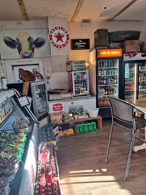 A cozy shop interior featuring shelves of groceries, a fridge with drinks, and vintage decor, including a gas station sign.