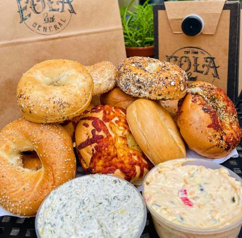A variety of bagels, including sesame and cheese, with two containers of creamy dip, arranged on a table.