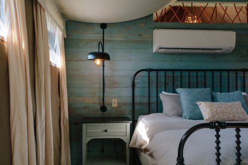 Cozy bedroom with a black metal bed, blue accent pillows, a nightstand, and a wall-mounted light against wooden walls.