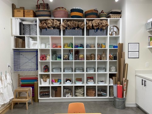 A neatly organized shelving unit filled with various craft supplies, baskets, and materials in a bright workspace.