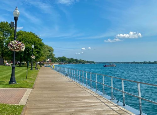 A scenic waterfront path lined with trees and flowers, overlooking a calm blue lake under a clear sky.
