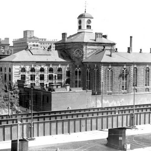 Historic building with a clock tower, featuring arched windows and a stone facade, set against a city backdrop.