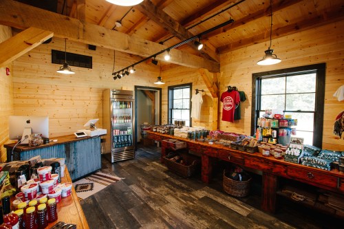 A cozy wooden shop interior with shelves of snacks, drinks, and merchandise, featuring rustic decor and warm lighting.