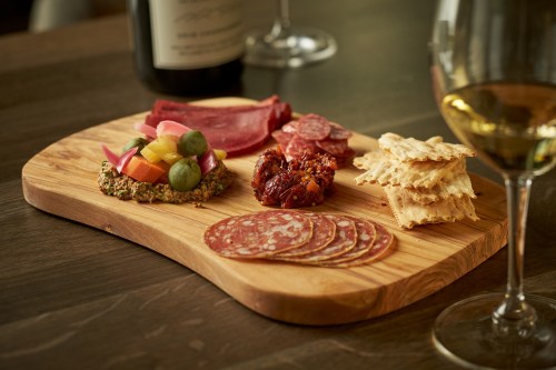 A wooden platter with assorted meats, cheeses, olives, and crackers, accompanied by a glass of white wine.