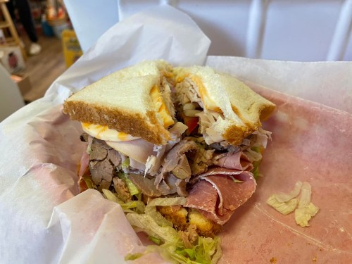 A hearty sandwich filled with various meats, lettuce, and cheese, served on white bread and wrapped in paper.