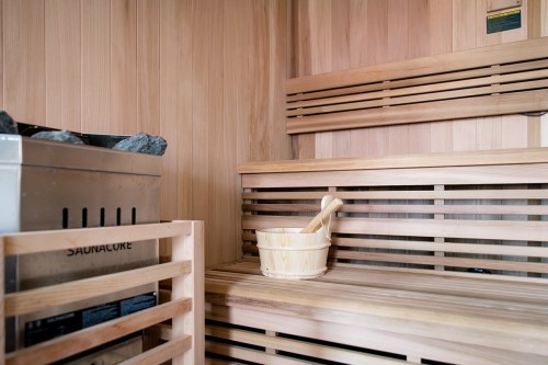 A wooden sauna interior featuring a stone heater, a wooden bucket, and a ladle on a bench.