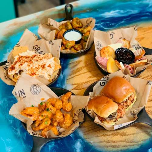 A colorful spread of five small dishes in cast iron pans, featuring appetizers and sliders on a wooden table.