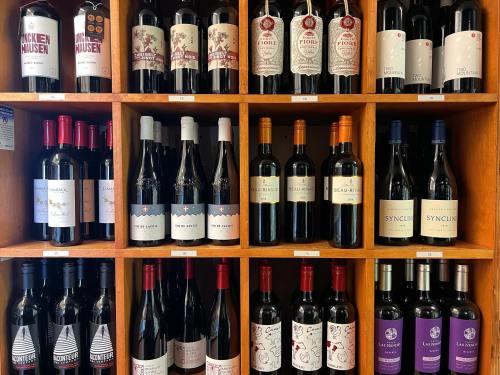 A wooden shelf displaying various bottles of red wine, organized by brand and label.