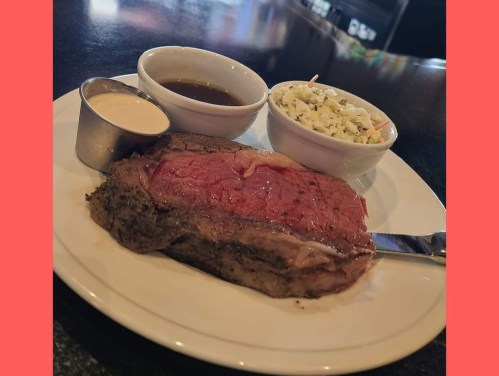 A plate with a juicy steak, two dipping sauces, and a side of coleslaw on a dark table.