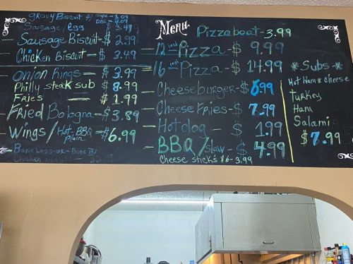Menu board featuring prices for various items: pizza, subs, wings, and sides, written in colorful chalk.