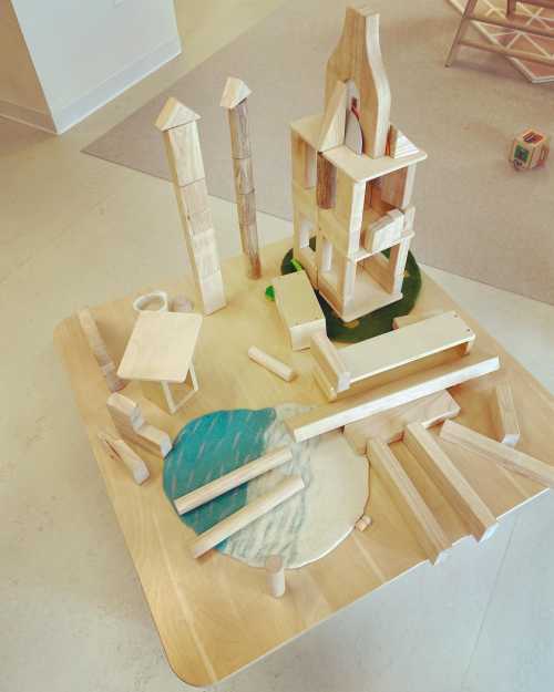 A wooden playset with various blocks arranged on a table, featuring a tower, pillars, and a circular base with water designs.