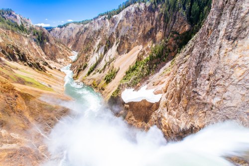 A stunning view of a waterfall cascading into a river, surrounded by rocky cliffs and lush greenery under a clear blue sky.