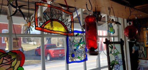 Colorful stained glass decorations hang in a window, with a red truck visible outside.