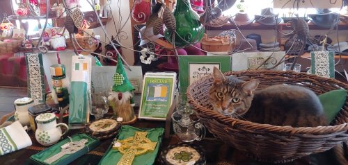 A tabby cat rests in a basket among various decorative items and St. Patrick's Day-themed decorations.