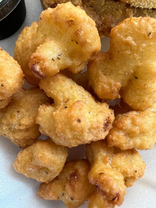 A close-up of golden-brown, crispy fried cauliflower bites on a white plate.