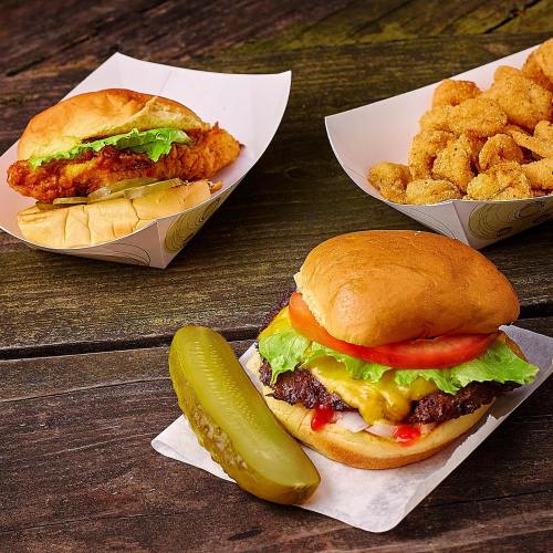 A burger with cheese and toppings, a chicken sandwich, and a side of crispy bites, with a pickle on the side.