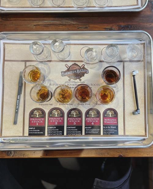 A tray with various whiskey samples, tasting notes, and a pen, set for a bourbon tasting experience.