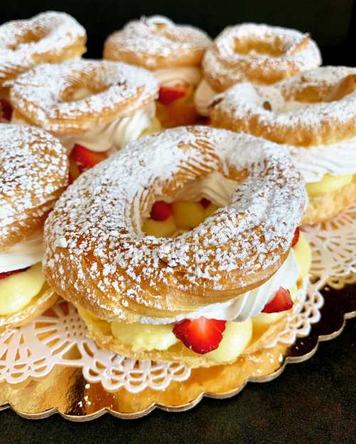 A close-up of cream-filled pastries topped with powdered sugar and fresh strawberries on a decorative platter.