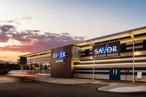 Exterior of River House building at sunset, featuring illuminated signs for "River" and "Savor at River House."