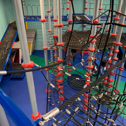 A colorful indoor climbing structure with ropes, nets, and various climbing elements for children to explore.