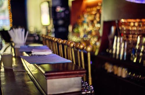 A dimly lit bar with a polished wooden counter and golden bar stools, featuring a blurred background of bottles.