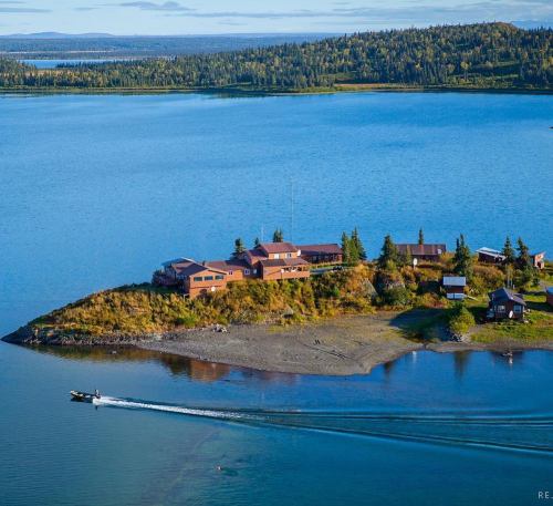 Aerial view of a small island with rustic buildings surrounded by calm blue water and lush green trees.