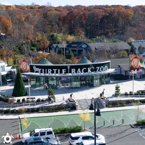 Aerial view of Turtle Back Zoo entrance with autumn foliage in the background and visitors walking around.