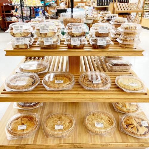 A wooden display shelf filled with various packaged baked goods, including pies and muffins, in a store.