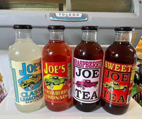 Four colorful bottles of beverages: classic lemonade, strawberry lemonade, raspberry tea, and sweet tea, displayed on a counter.