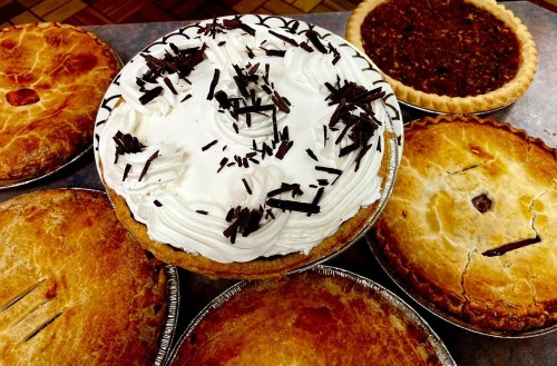 A variety of pies, including a cream pie topped with whipped cream and chocolate shavings, on a table.