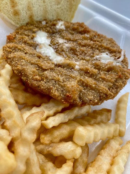 A crispy fried chicken patty with melted butter, served with crinkle-cut fries in a takeout container.
