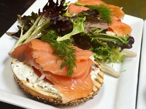 A toasted bagel topped with cream cheese, smoked salmon, and fresh dill, served with a side of mixed greens.