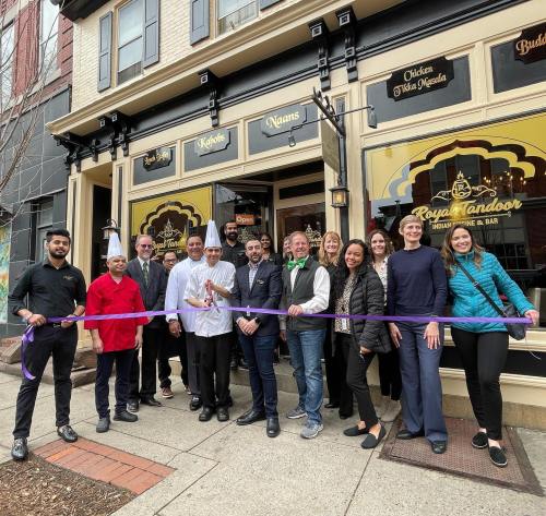 A group of people, including chefs and staff, celebrate the opening of Royal Tandoor restaurant with a ribbon-cutting ceremony.