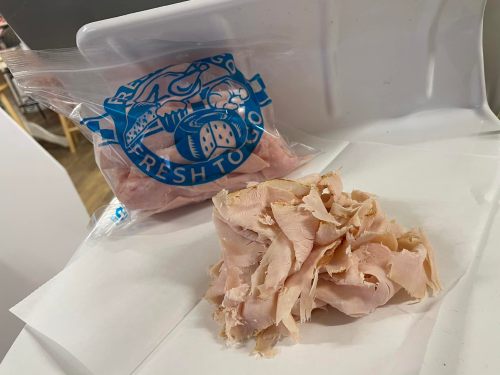 A bag of sliced turkey breast next to a pile of shredded turkey on a white surface.