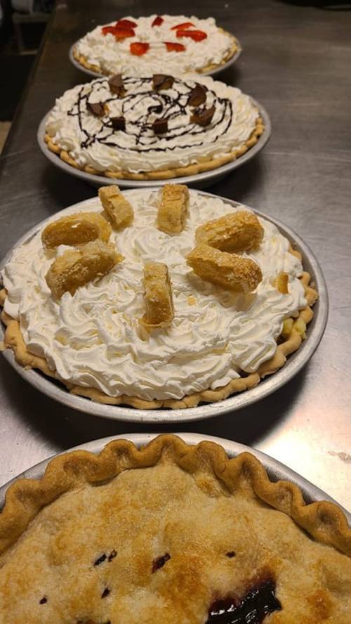 Four pies lined up on a table, topped with whipped cream, fruit, and decorative toppings.