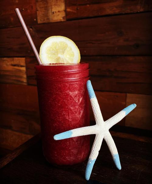 A vibrant red drink in a jar with a straw and a lemon slice, next to a blue and white starfish on a wooden surface.
