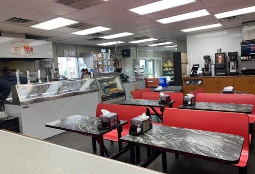 Interior of a casual eatery with red tables, a counter displaying ice cream, and a self-service drink station.