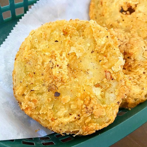 Two golden-brown, crispy fried green tomato slices on a green basket lined with parchment paper.