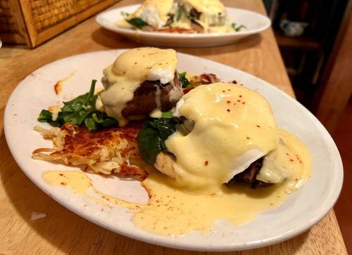A plate of eggs Benedict with spinach, hollandaise sauce, and hash browns, served on a wooden table.
