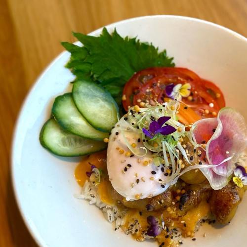 A vibrant bowl of food featuring a poached egg, fresh vegetables, and edible flowers on a wooden table.