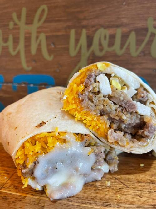 A close-up of a cut burrito filled with cheese, sausage, and scrambled eggs, resting on a wooden surface.