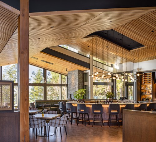 Modern bar interior with wooden accents, stylish seating, and large windows overlooking greenery. Warm, inviting atmosphere.