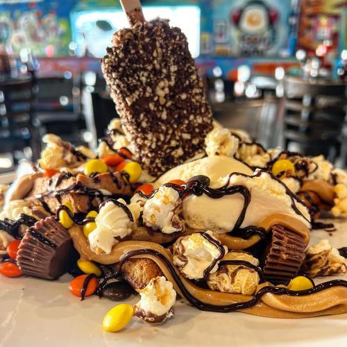 A decadent dessert featuring ice cream, popcorn, chocolate drizzle, candy, and a chocolate-covered treat on top.