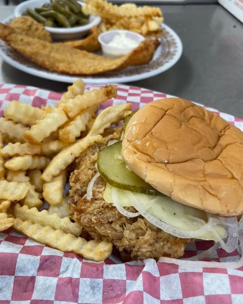 A crispy chicken sandwich with pickles and onions, served with crinkle-cut fries on a red and white checkered paper.