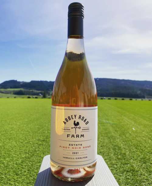 A bottle of Abbey Road Farm 2021 Estate Pinot Noir Rosé on a grassy field with hills in the background.