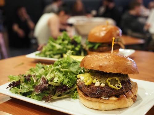 A close-up of a burger with toppings on a plate, accompanied by a side of mixed greens in a casual dining setting.