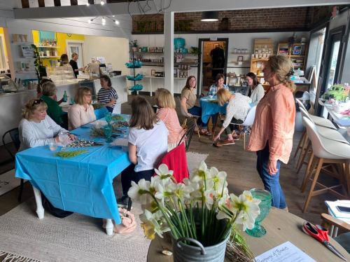 A group of people gathered around tables in a bright, cozy space, engaged in a crafting activity.